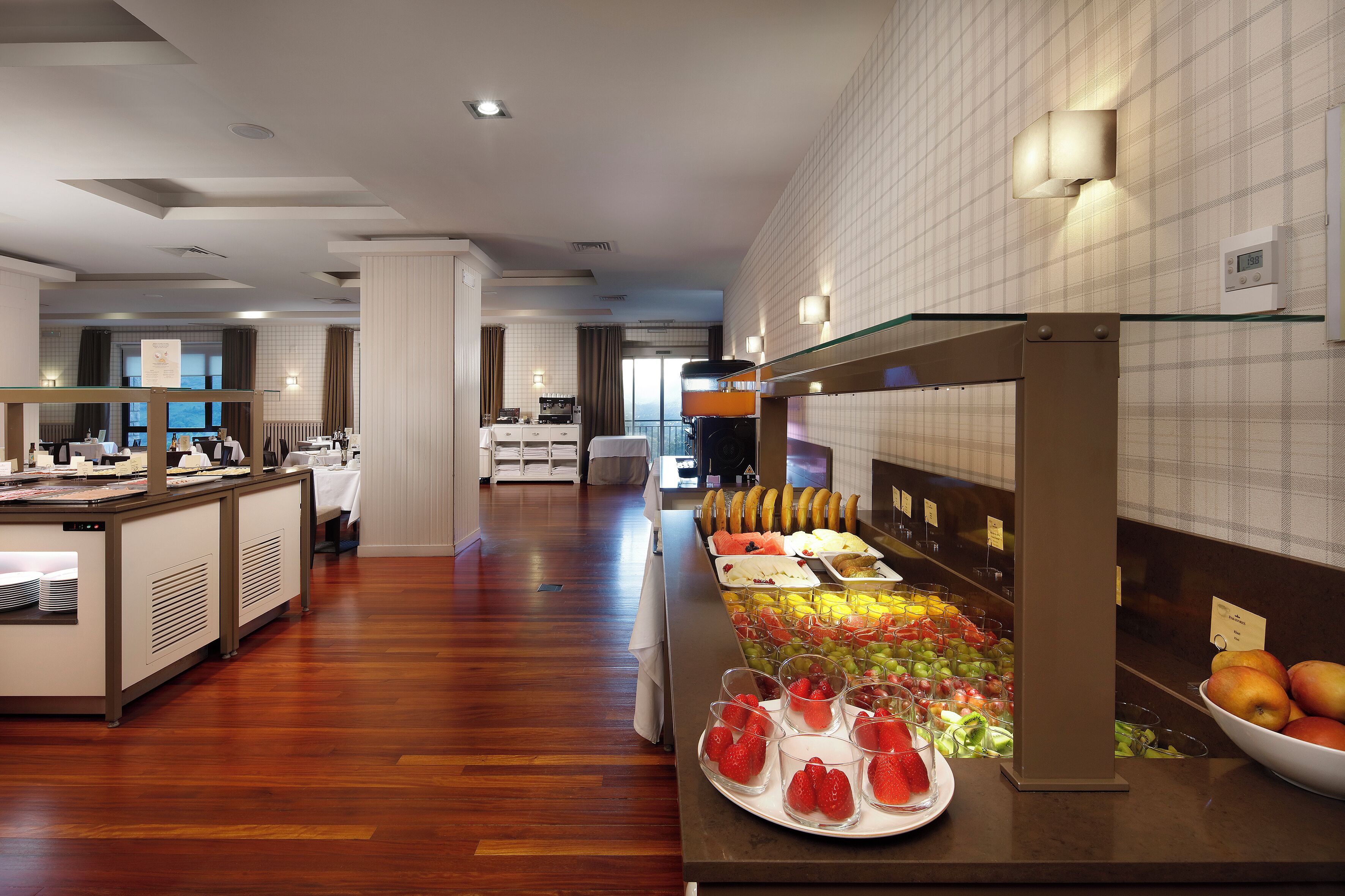 A buffet area with a variety of fruits and vegetables, a counter with a glass top, and a seating area in the background.