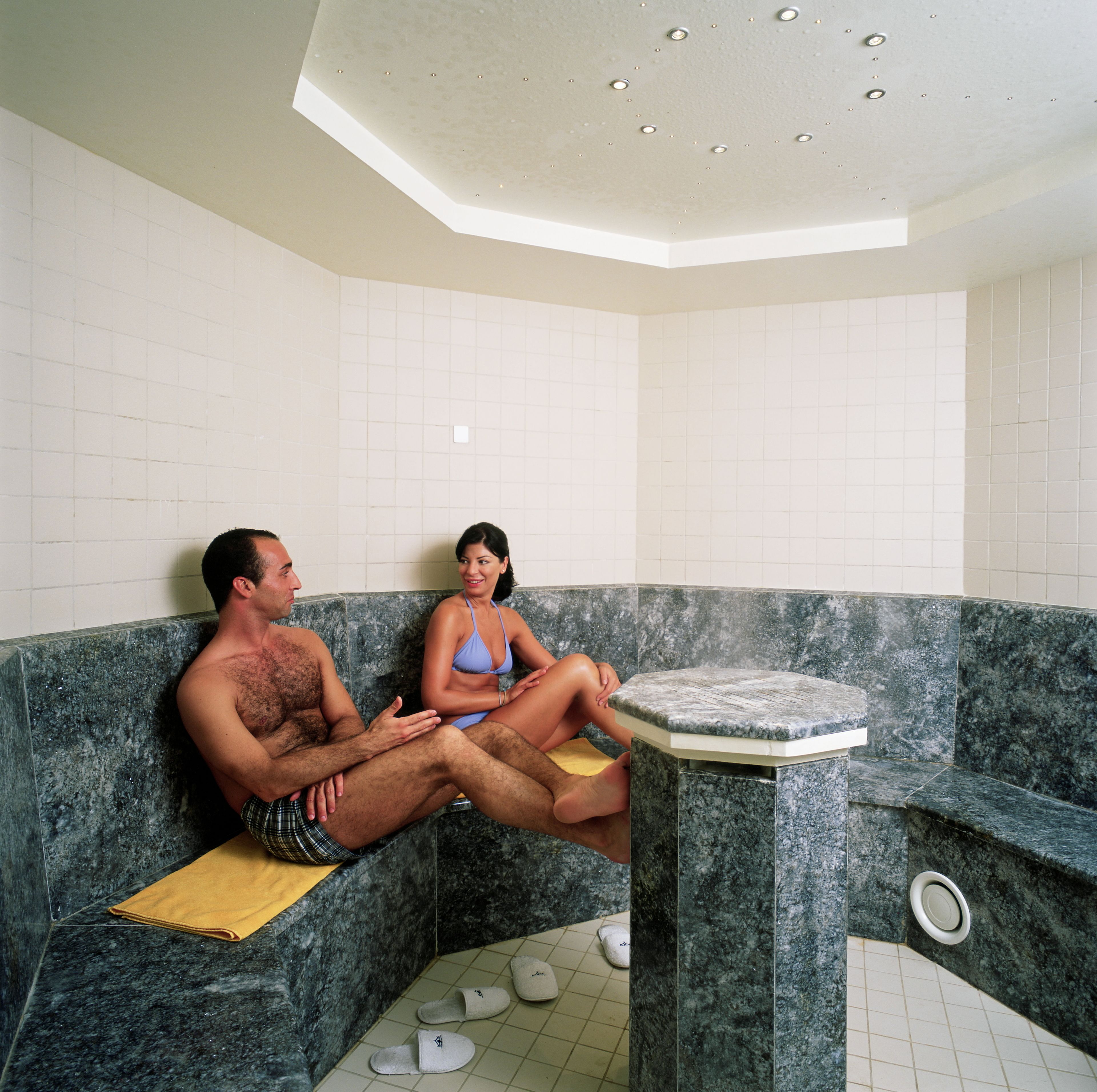 A couple sitting in a spa-like setting with a marble bench and a small table.