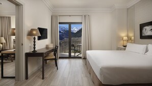 A hotel room with a bed, a desk, a chair, a table, a lamp, a painting, a window with a mountain view, and a sliding door. - Parador De Vielha Spa & Wellness (Vielha e Mijaran)