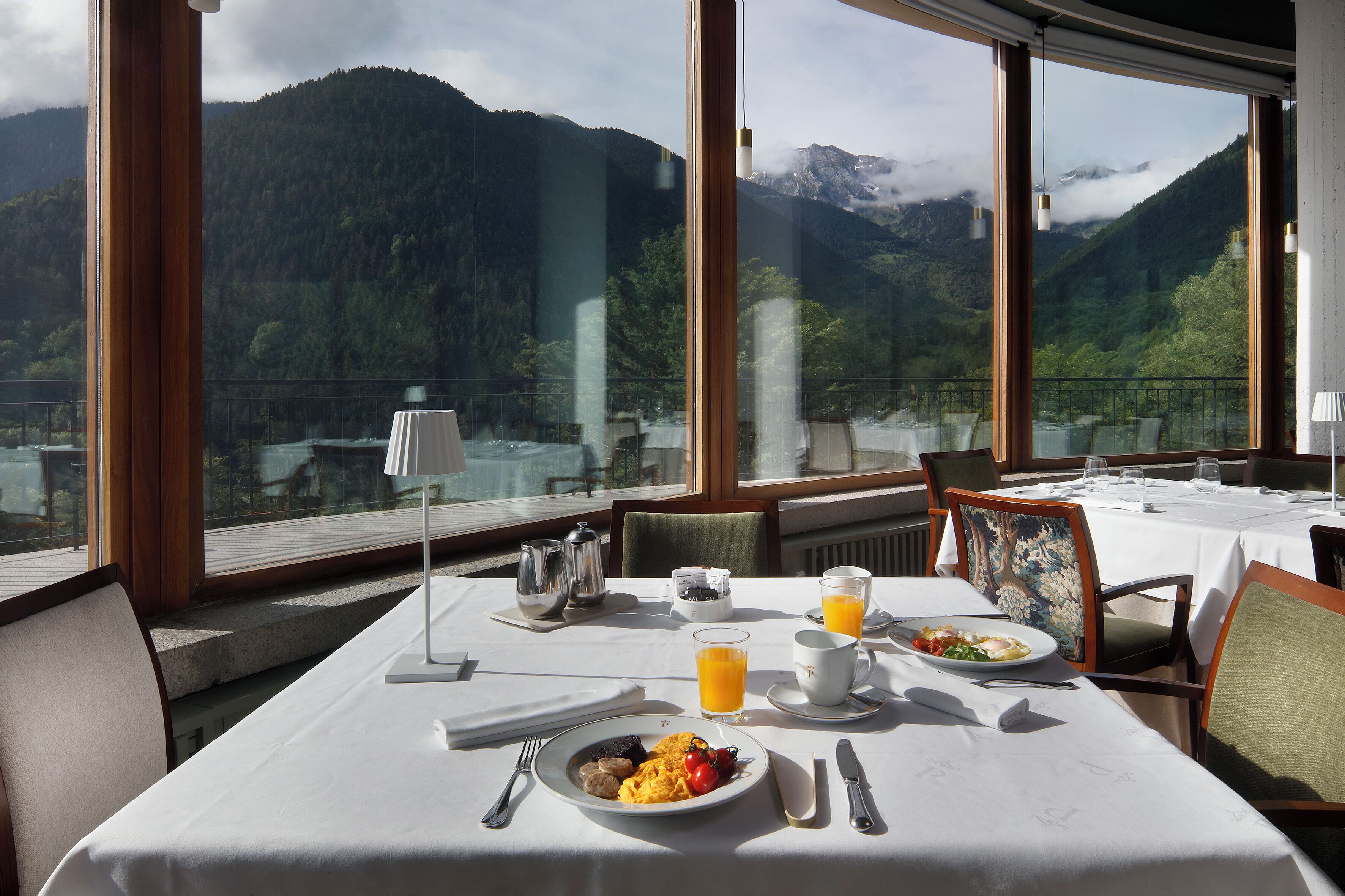 A dining table set with breakfast, a view of mountains, and a large window.