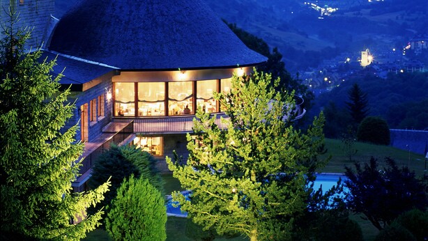 A house with a thatched roof, large windows, and a view of mountains in the background. - Parador De Vielha Spa & Wellness (Vielha e Mijaran)