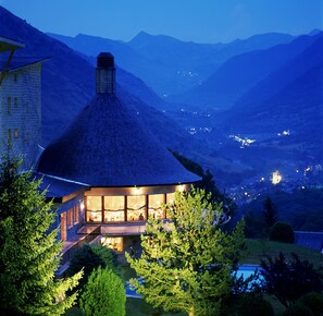 Ein Haus mit einem Strohdach, großen Fenstern und Blick auf Berge im Hintergrund.