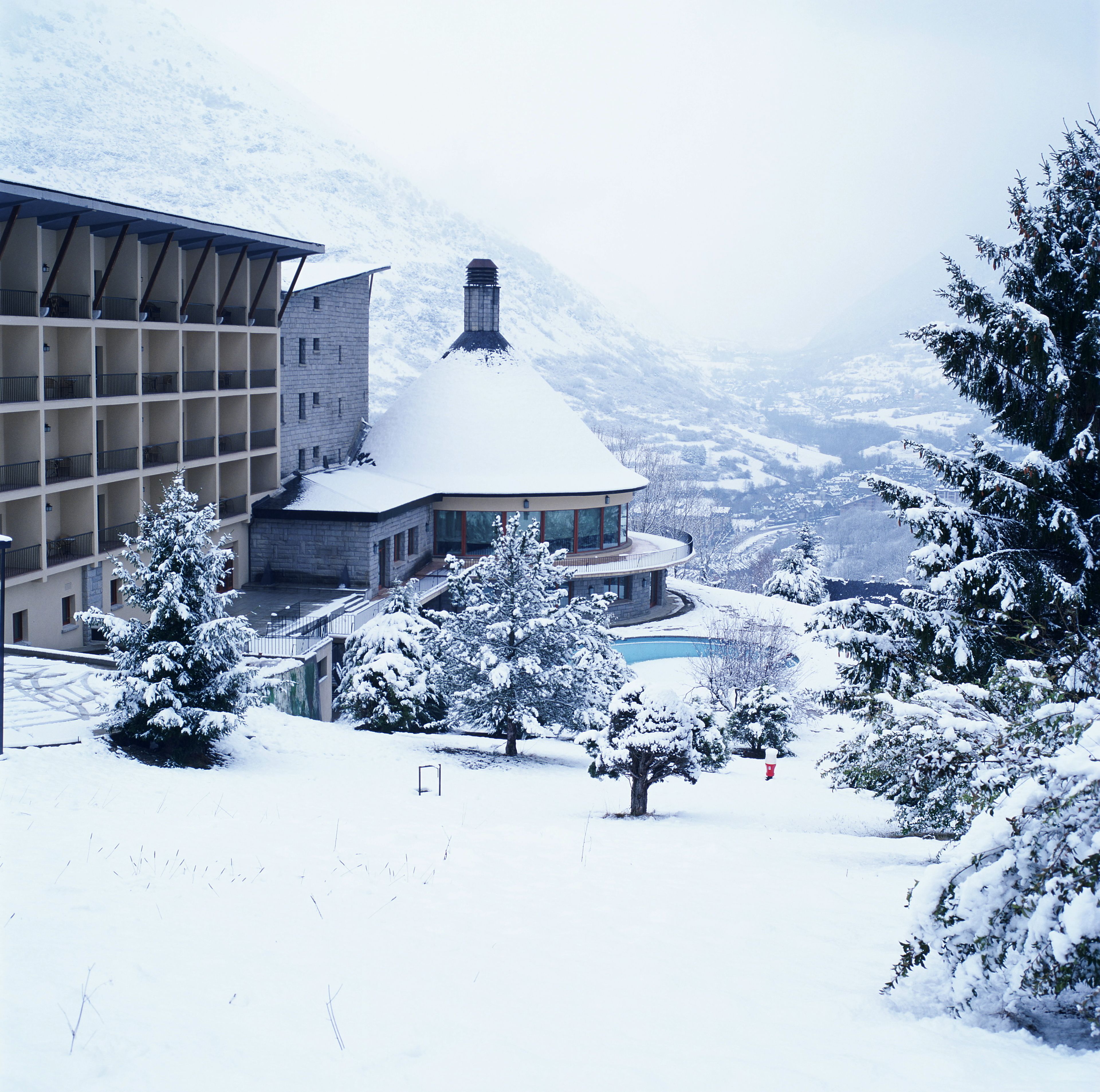 A hotel with a snow-covered roof, a pool, and a mountainous backdrop.