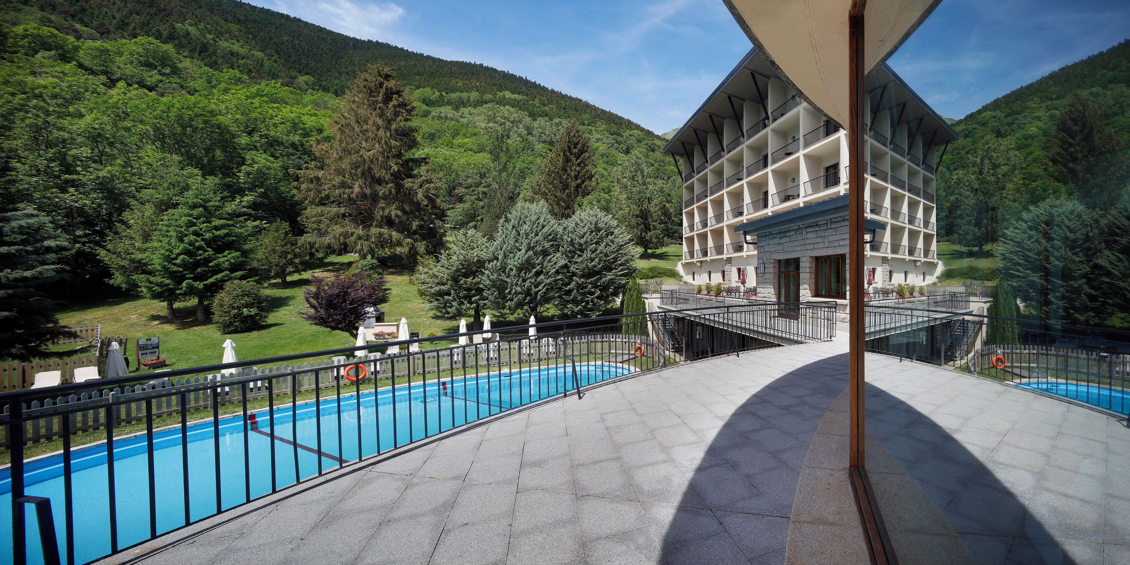 A hotel with a pool, surrounded by lush greenery and mountains.