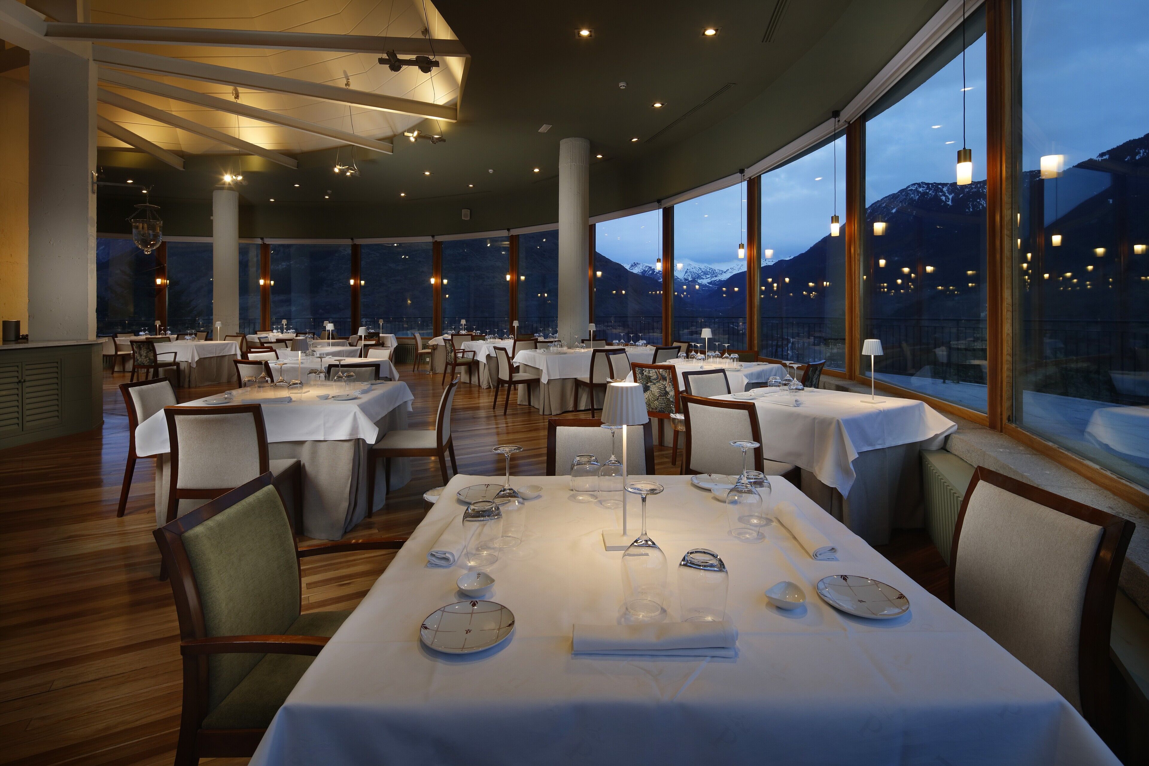 Un restaurant où les tables sont dressées pour le service, avec de grandes fenêtres offrant une vue sur les montagnes et un décor intérieur moderne.