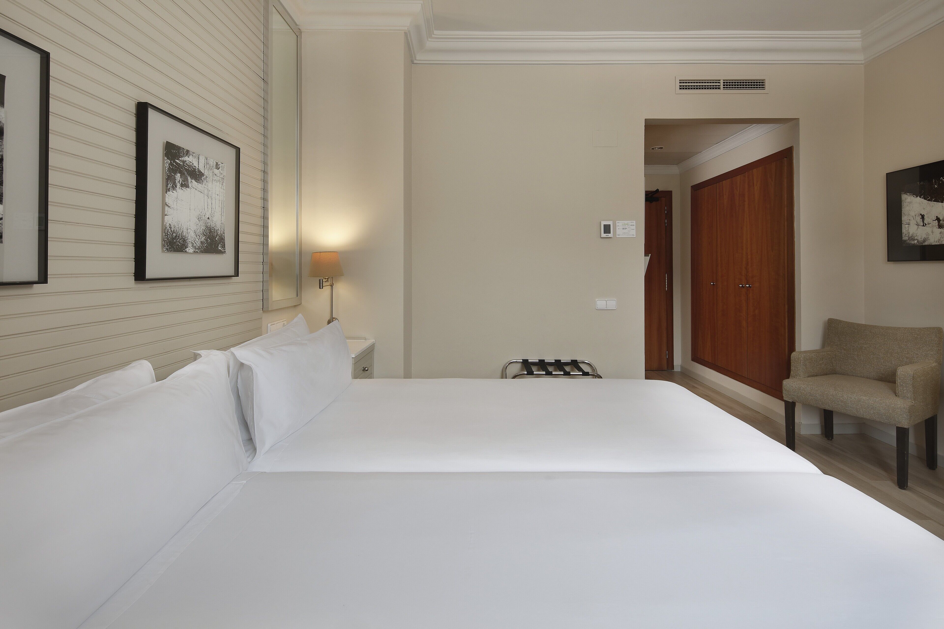 Una habitación de hotel con una cama grande, una silla, una mesita de noche y una lámpara fijada a la pared.