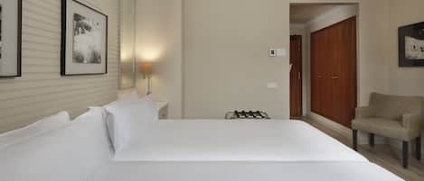 A hotel room with a large bed, a chair, a nightstand, and a wall-mounted lamp.