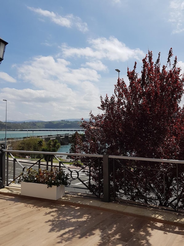 A balcony with a view of a bridge, a body of water, and distant hills.