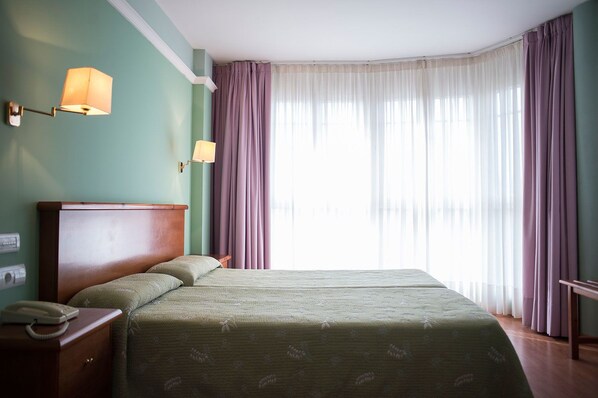 A hotel room with a double bed, two bedside lamps, a bedside telephone, and a window with sheer curtains. - Faro de San Vicente (San Vicente de la Barquera)