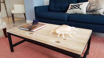 Un salon avec un canapé bleu foncé, une table basse en bois sur laquelle se trouvent un livre et un objet décoratif, et un tapis à motifs représentant des harengs rouges.