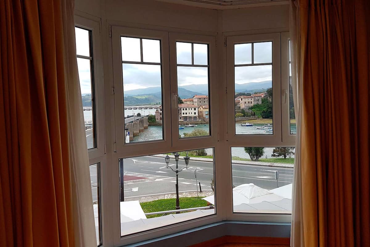 A bay window with a view of a river, buildings, and a bridge.