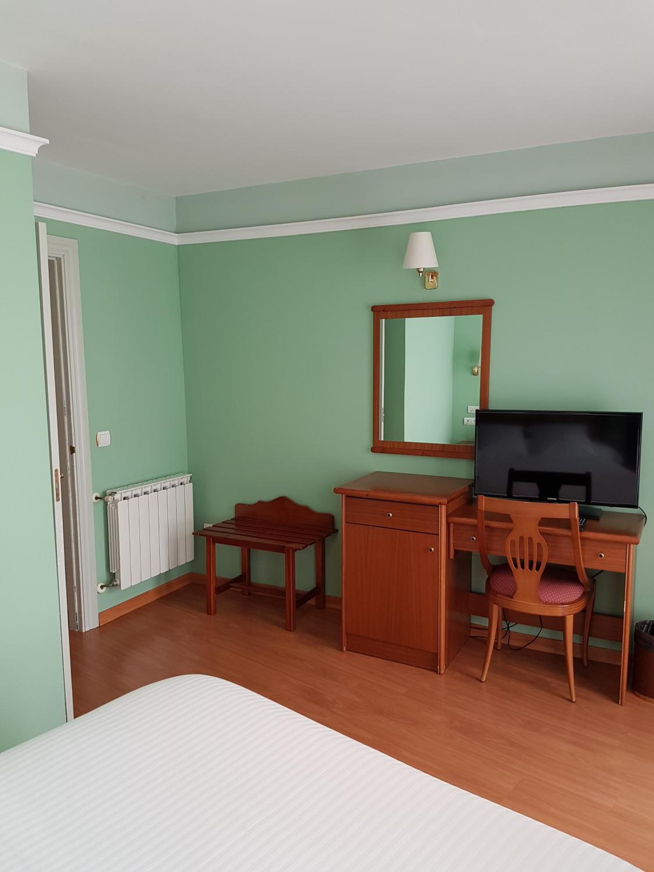 A room with a bed, a desk with a chair, a radiator, and a television.