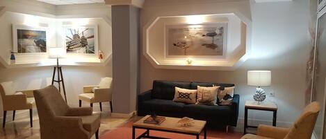A modern living room with a black sofa, beige armchairs, a coffee table, and artwork on the walls.