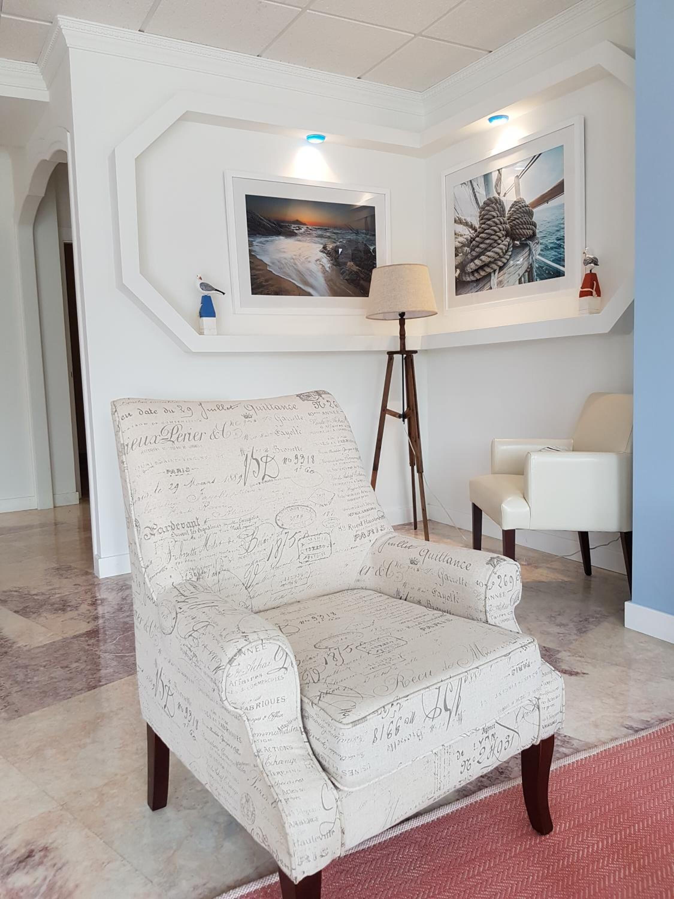 Una habitación con un sillón estampado, una lámpara de pie y dos cuadros en la pared.