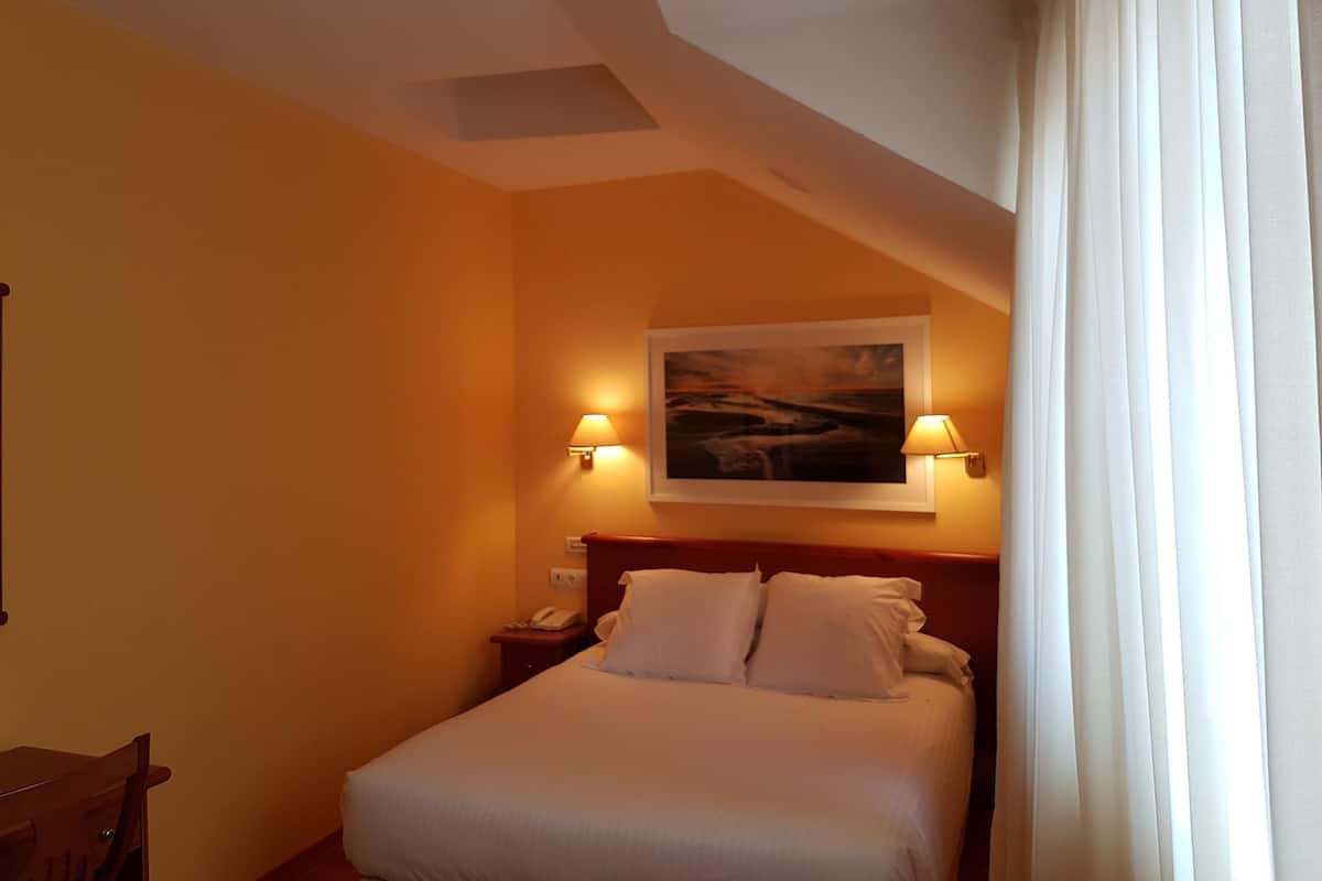 A hotel room with a bed, two bedside lamps, a painting on the wall, and a telephone on the nightstand.