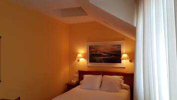 A hotel room with a bed, two bedside lamps, a painting on the wall, and a telephone on the nightstand.