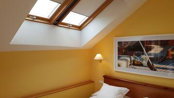 A bedroom with a skylight, a bed, a wall-mounted lamp, and a framed picture.