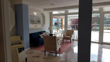 Un vestíbulo amplio con un sofá azul, un sillón beige y un sillón blanco. Se aprecia una ventana grande con vistas al exterior.