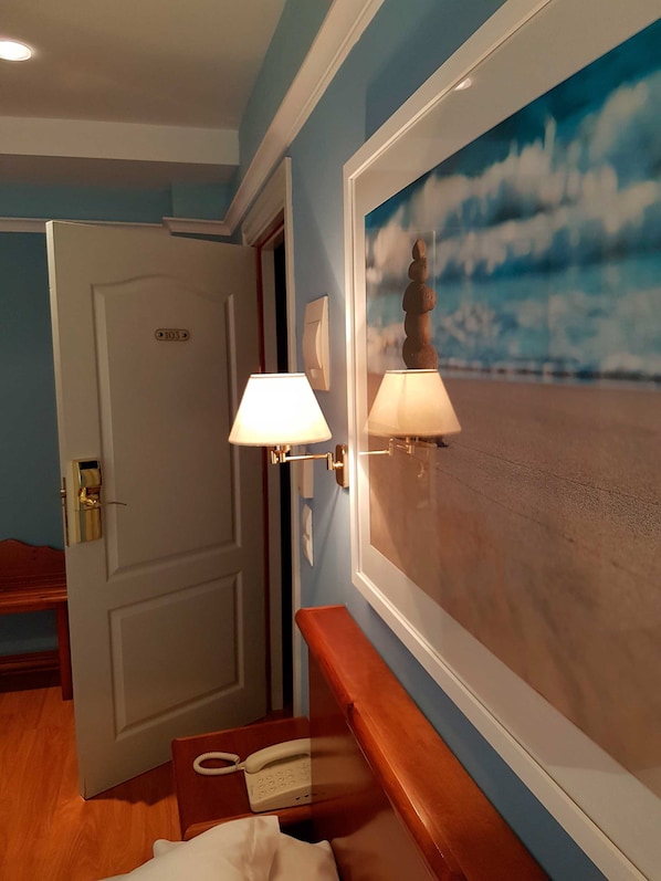 A hotel room with a wooden bench, a telephone, and a painting of a beach scene. - Faro de San Vicente (San Vicente de la Barquera)