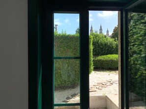 A view through a window with a stone pathway and greenery, leading to a building with multiple spires. - Pombal Rooms (Santiago de Compostela)