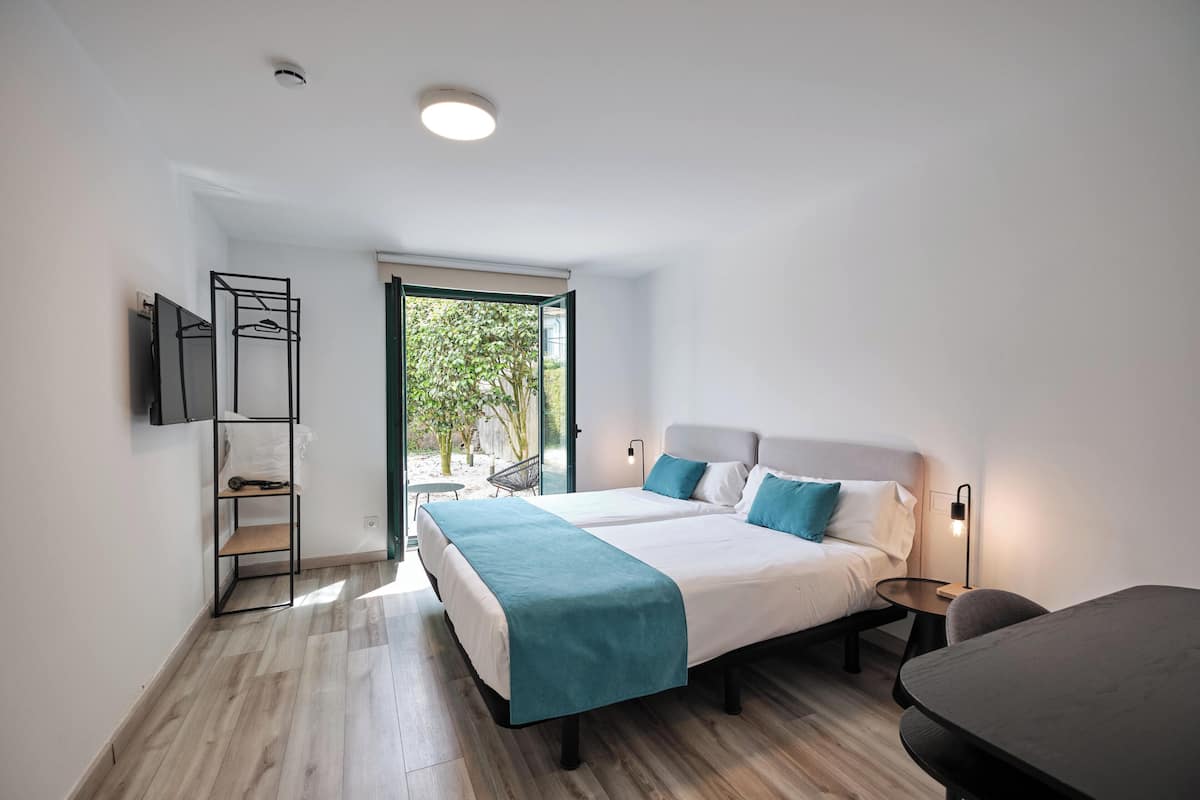 Quarto moderno com uma cama grande, mesas de cabeceira, uma mesinha e uma TV fixada na parede.