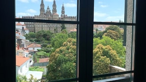 Vista a través de una ventana con balcón, mostrando un edificio histórico con dos torres al fondo.