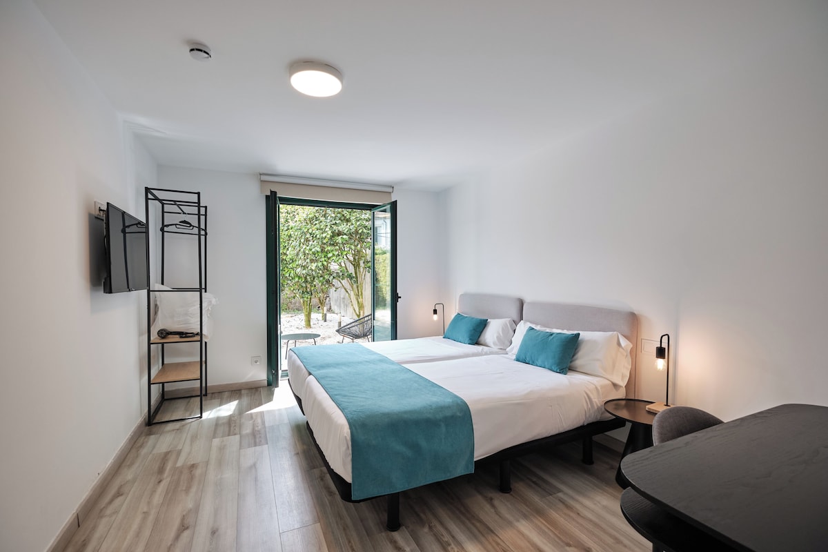 A modern bedroom with a large bed, bedside tables, a small table, and a TV mounted on the wall.