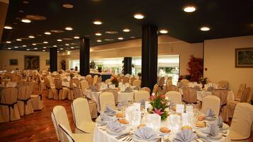 Un salón de banquetes con mesas redondas dispuestas para un evento formal, con manteles blancos, cubiertos de plata y centros de mesa florales.
