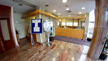 Una zona de recepción con un mostrador de madera, un letrero azul con una 'T' blanca y una alfombra estampada.