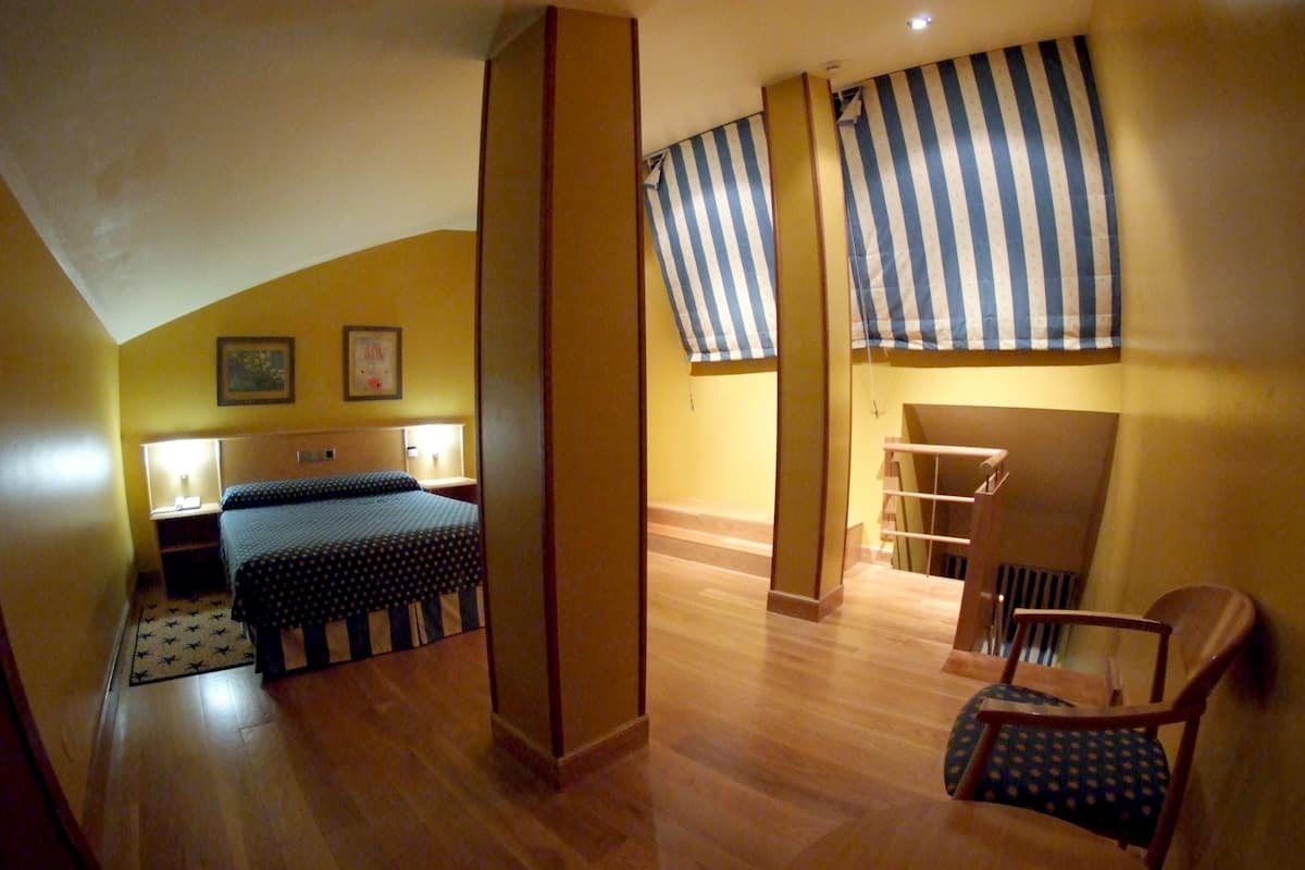 Quarto com uma cama, uma cadeira, uma escrivaninha e uma escada.