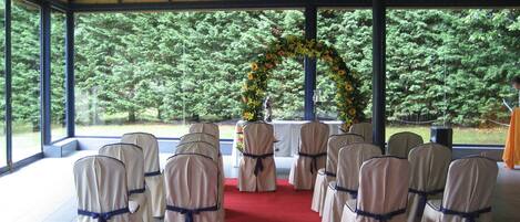 Uma área externa coberta com fileiras de cadeiras dispostas para um evento, tapete vermelho e um arco floral.