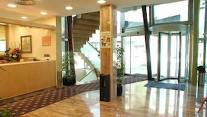 Un vestíbulo de hotel con mostrador de recepción, una escalera y entrada por puerta de vidrio.