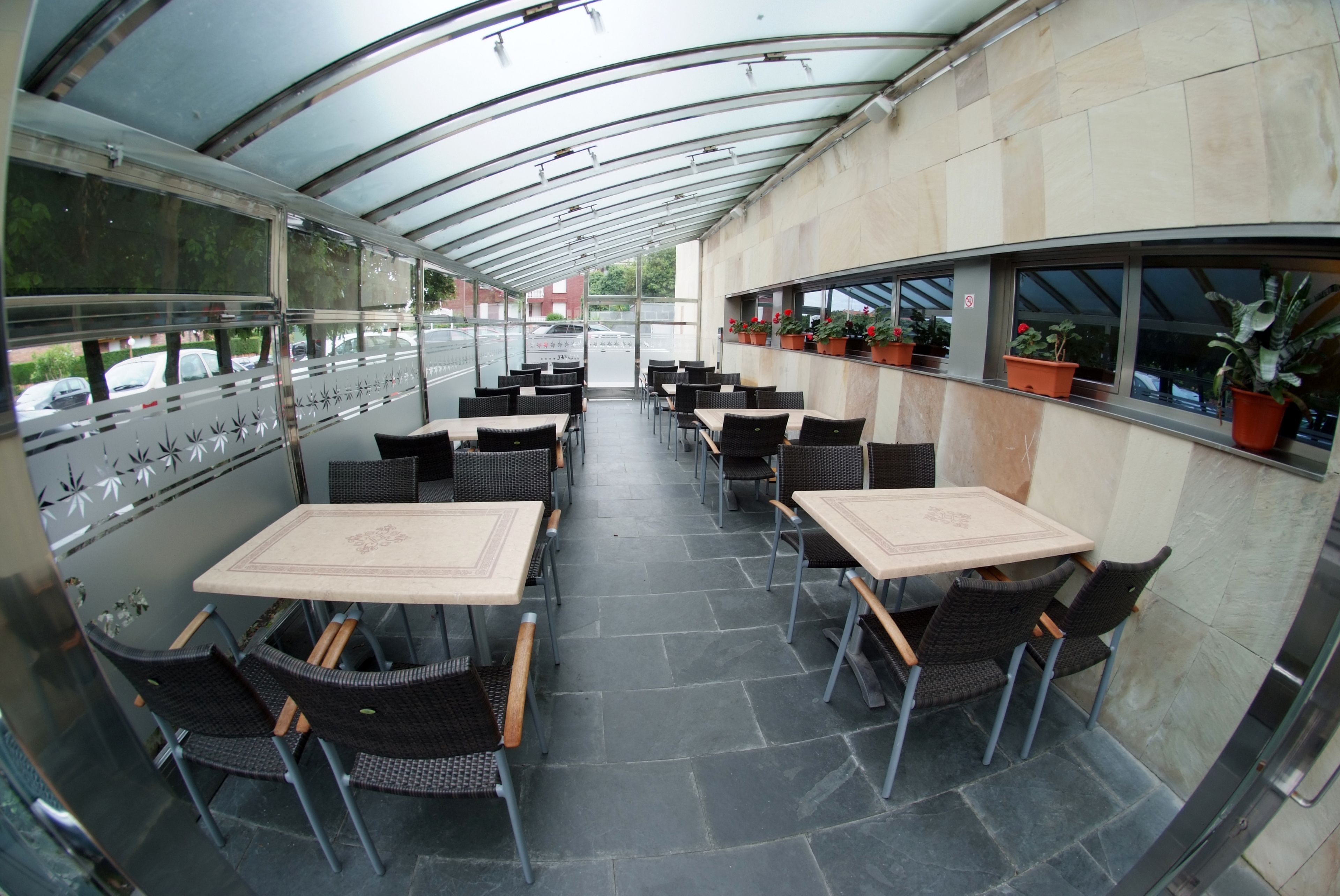 A covered outdoor seating area with tables and chairs, potted plants, and a view of the street.