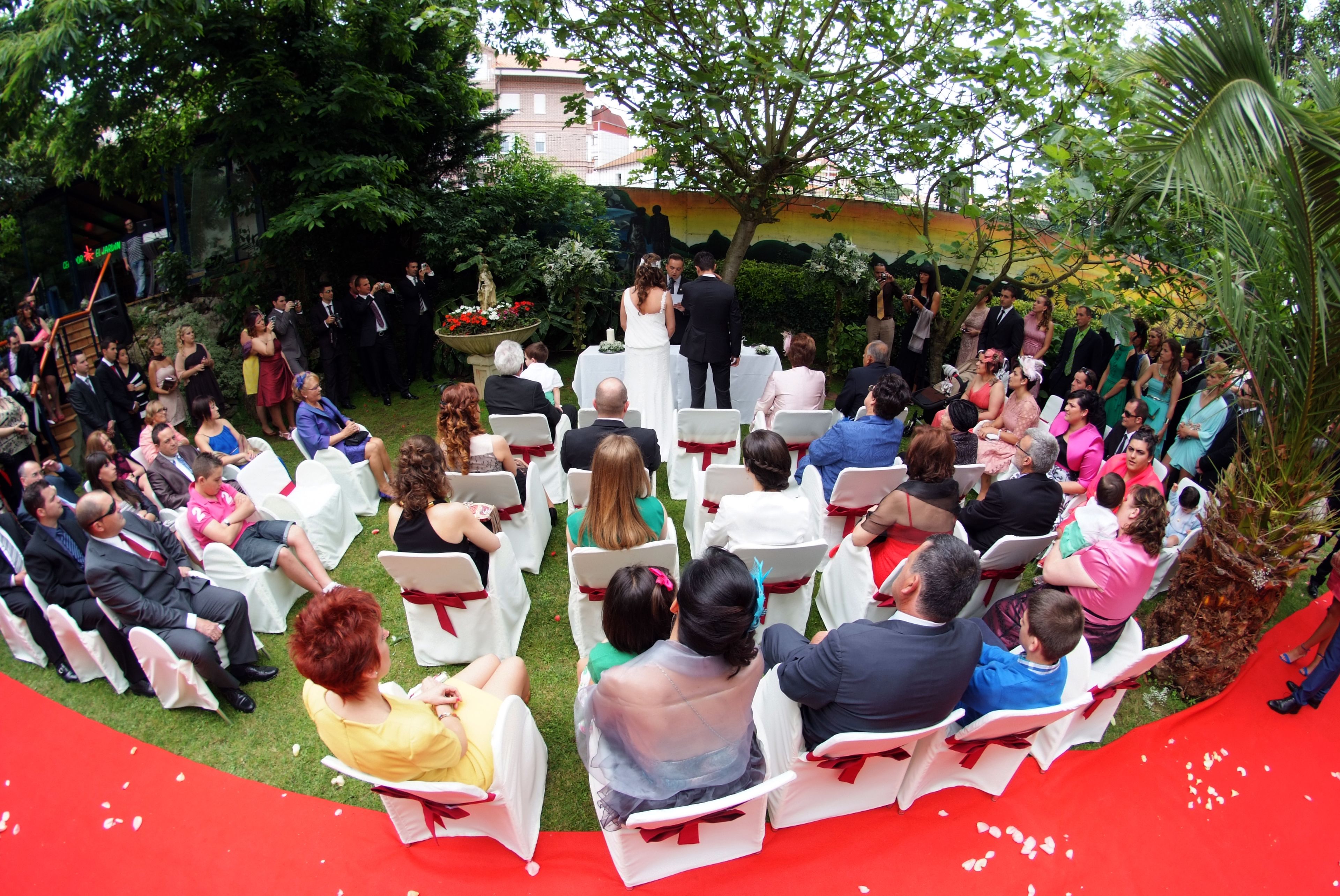 An outdoor wedding ceremony with guests seated in rows of white chairs, facing a couple at the altar.