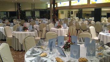 Uma sala de banquetes com mesas redondas dispostas para um evento formal, incluindo talheres, louças e centros de mesa florais.