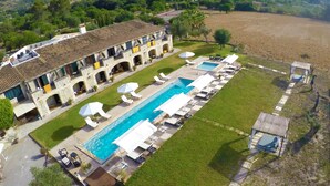 A large pool with sun loungers and umbrellas, surrounded by a well-maintained lawn and a stone building with multiple balconies.