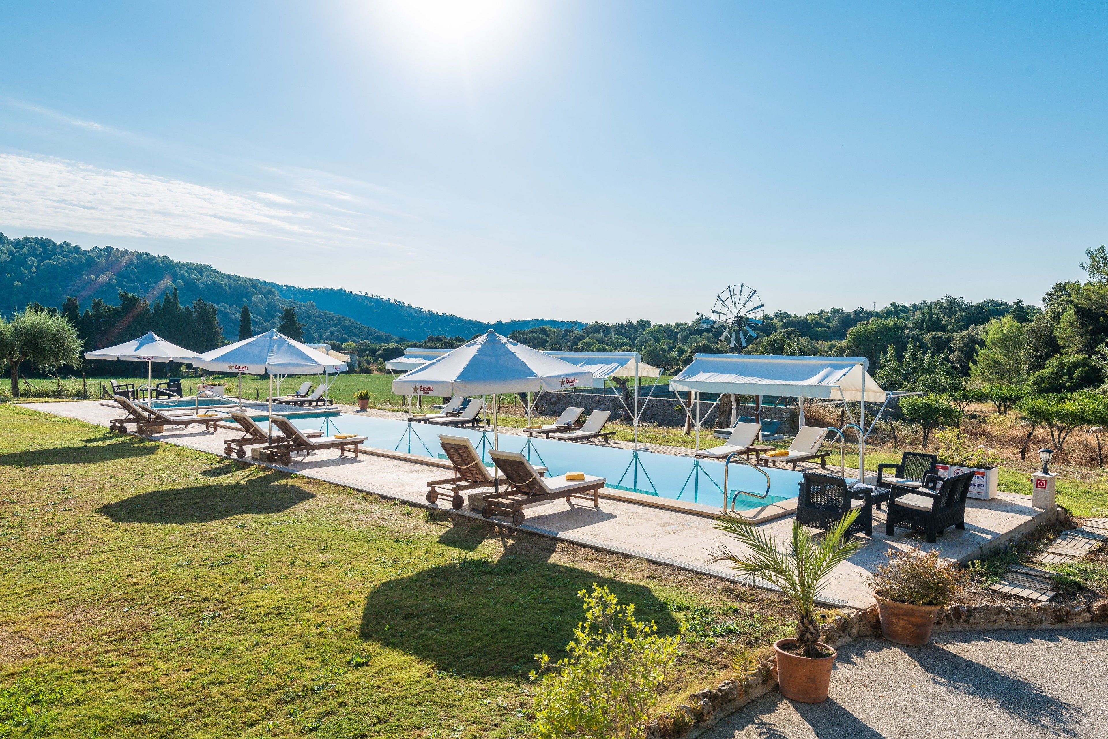 A pool area with lounge chairs and umbrellas, surrounded by a grassy landscape and hills.