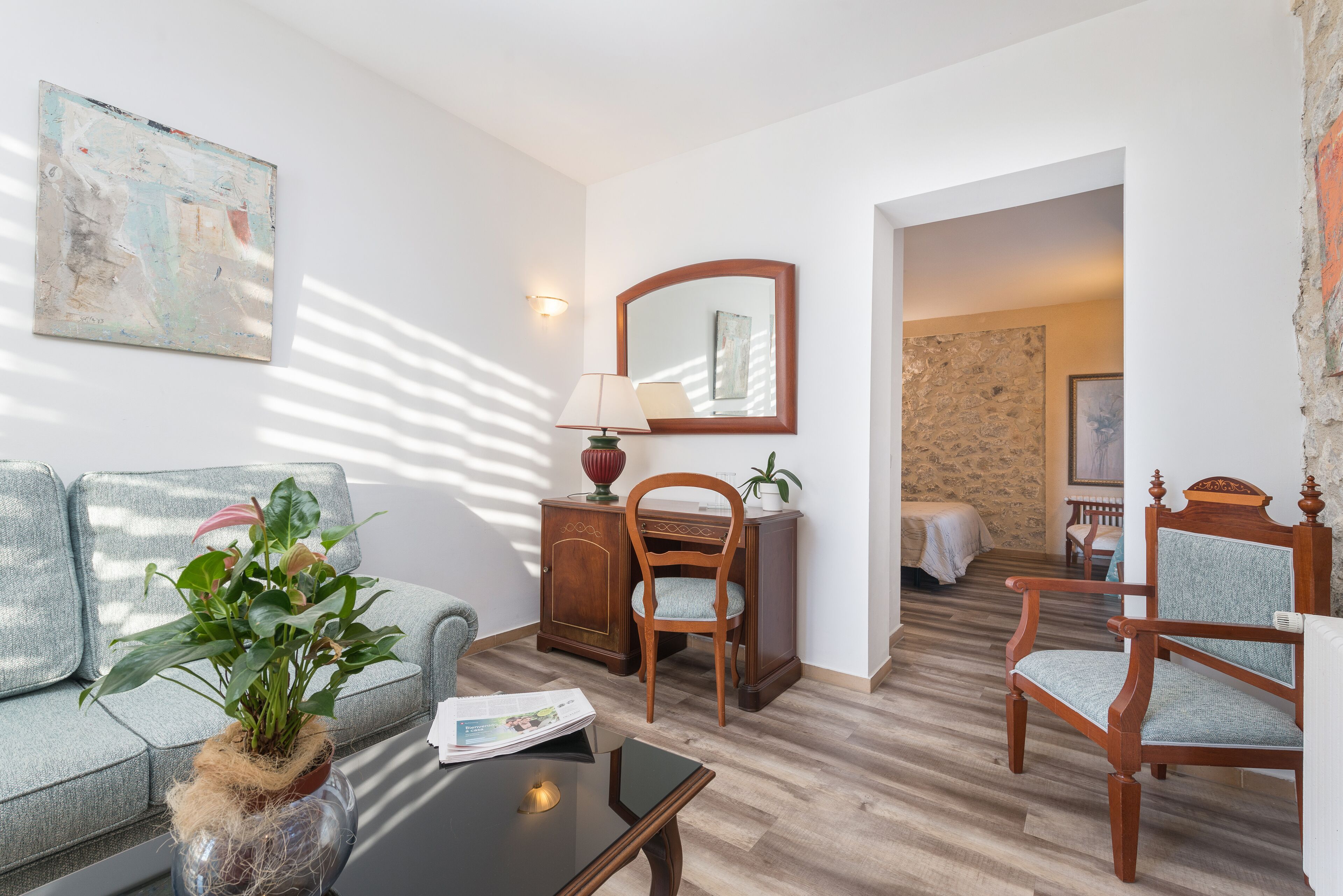 Una habitación con un sofá, una silla de madera, una mesita, una lámpara, un espejo y una planta.