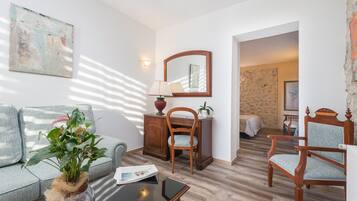 Una habitación con un sofá, una silla de madera, una mesita, una lámpara, un espejo y una planta.