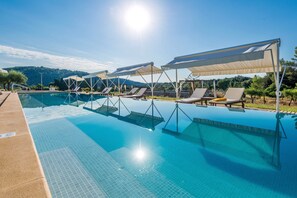 Une piscine dotée de chaises longues et de parasols, entourée d’un espace paysager aménagé et offrant une vue sur les collines.