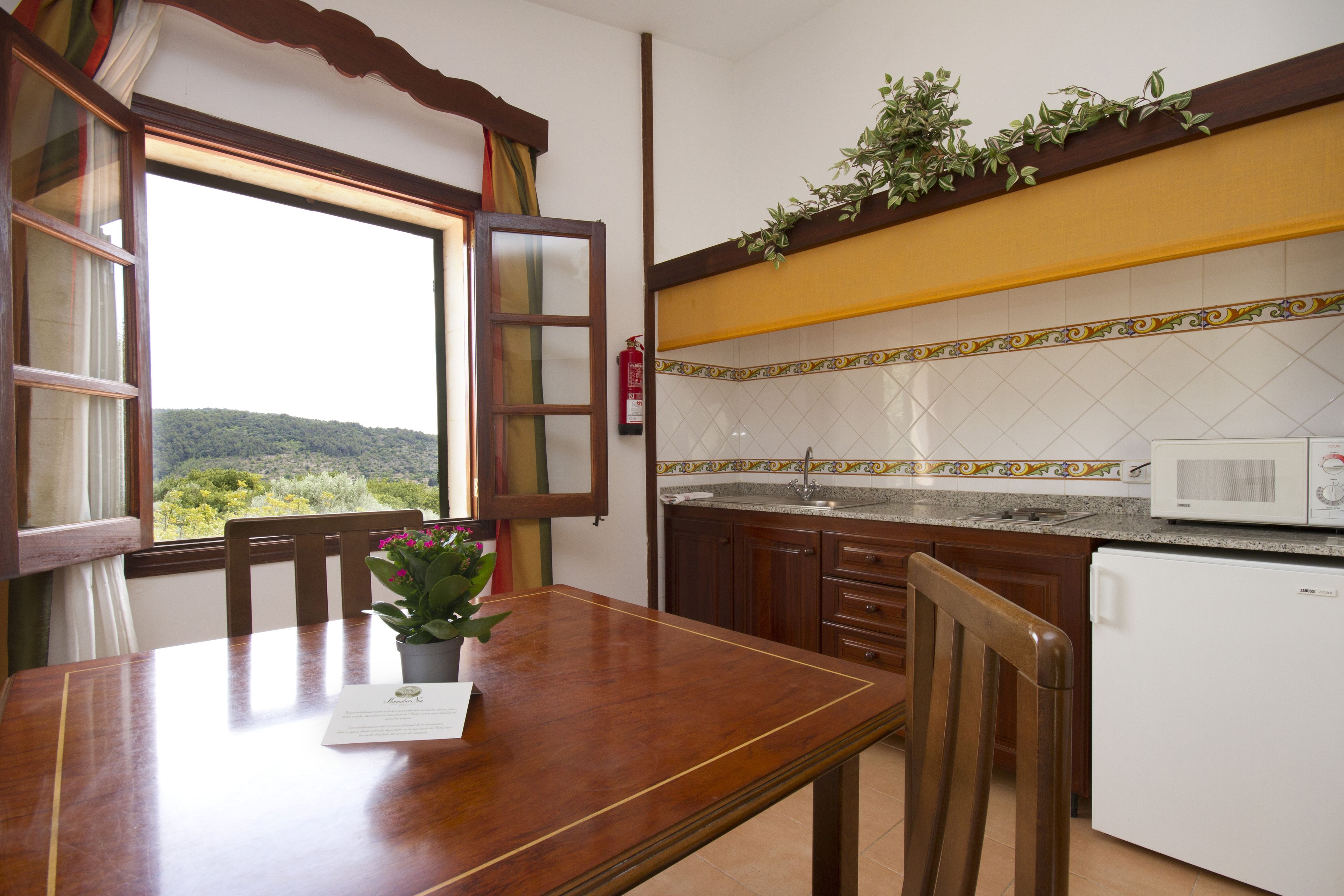 A kitchen with a wooden table, a potted plant, a microwave, and a view of the outdoors.