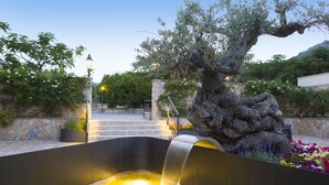 A water feature with a stone statue, a stone wall, and a staircase leading up to a building.