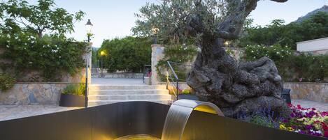 Un élément décoratif aquatique agrémenté d’une statue en pierre, d’un mur en pierre et d’un escalier menant à un bâtiment.