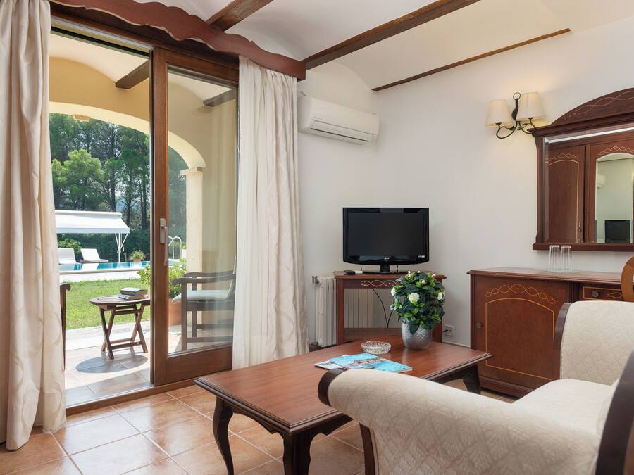Una habitación con televisión, un armario de madera, una mesa con una revista y vistas a una piscina exterior.
