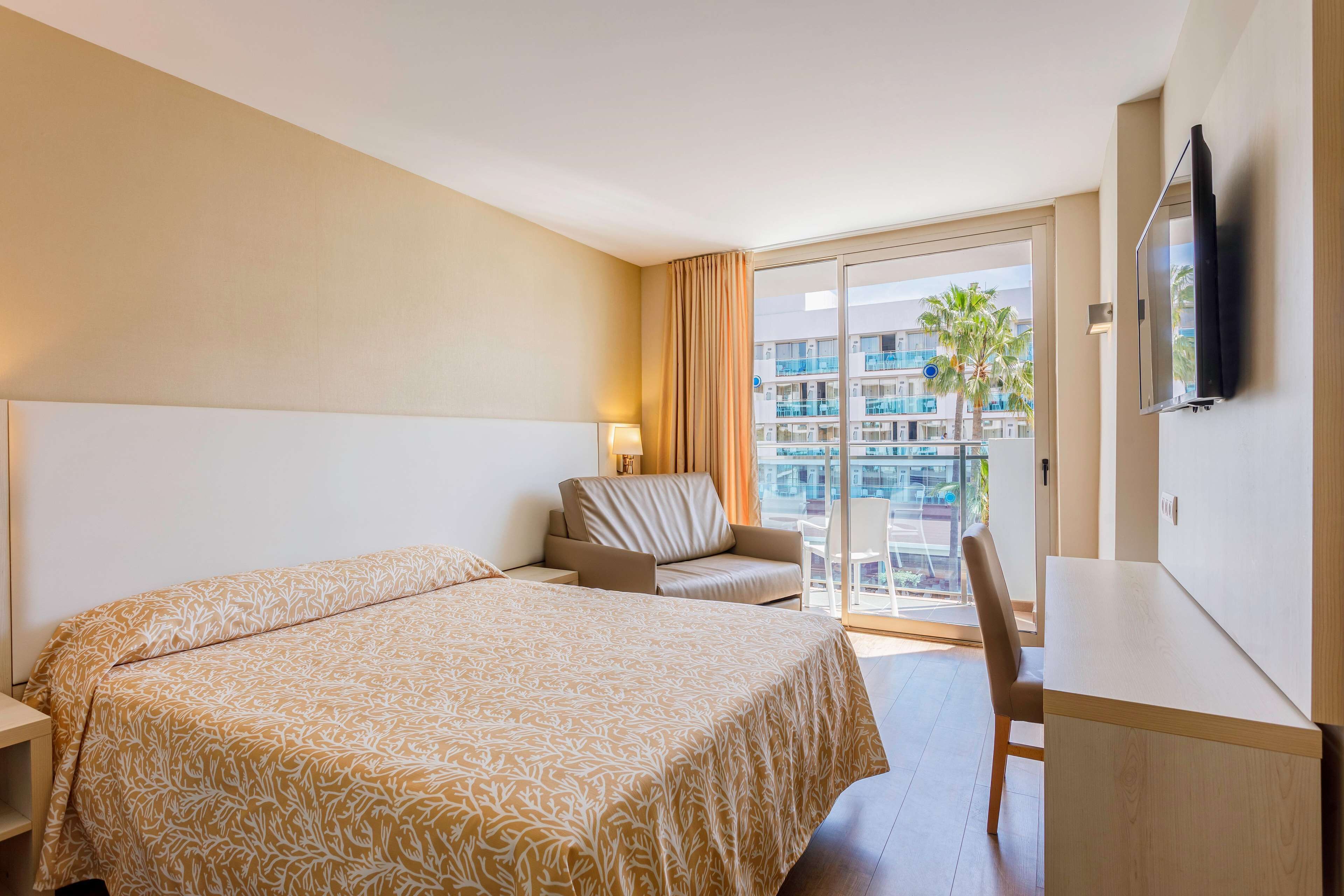 A hotel room with a large bed, a desk, a chair, and a TV.