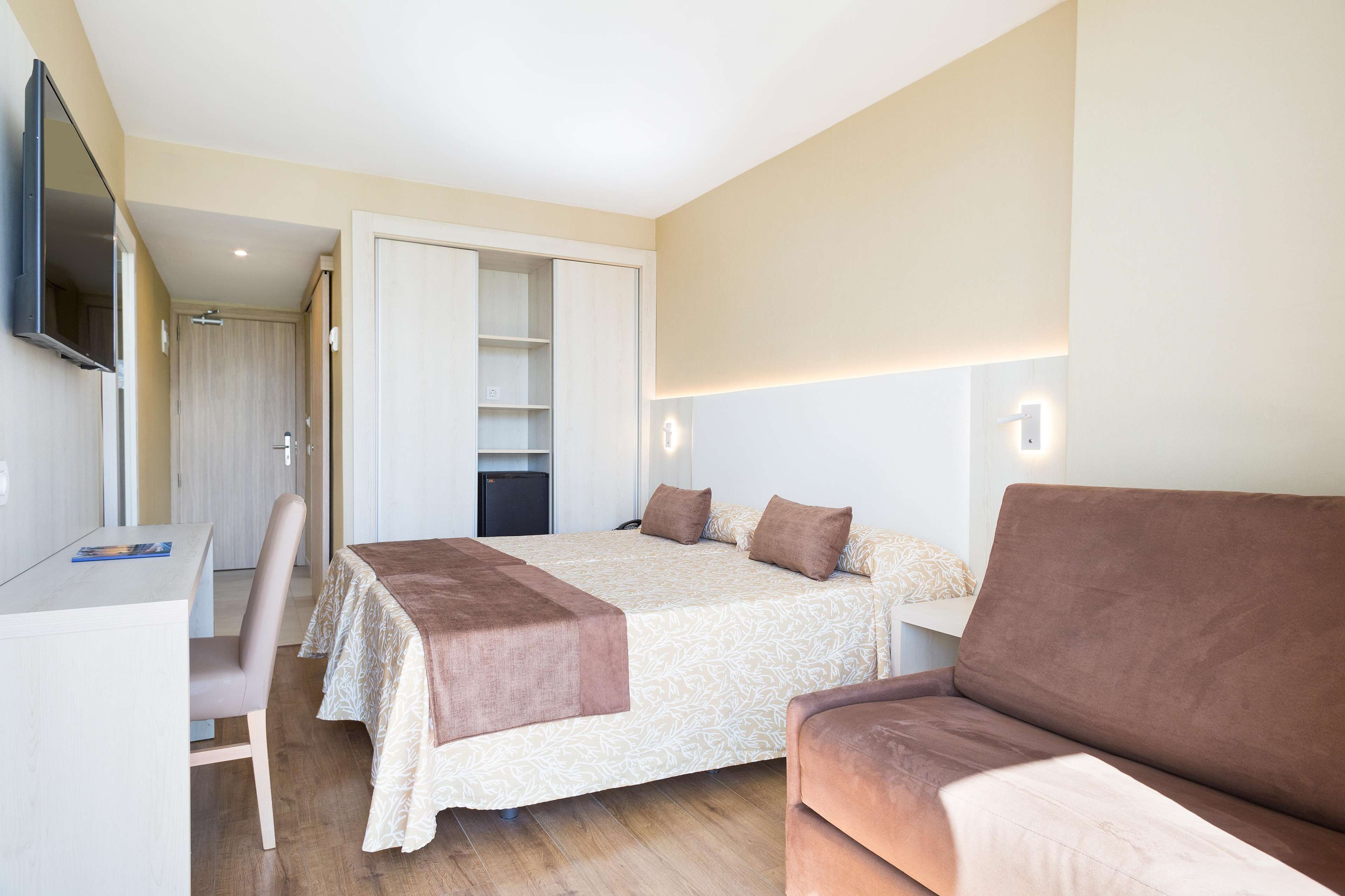 Een slaapkamer met een bed, een bureau, een stoel, een bank en een tv die aan de muur is bevestigd.
