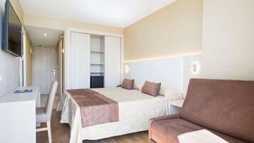 Een slaapkamer met een bed, een bureau, een stoel, een bank en een tv die aan de muur is bevestigd.
