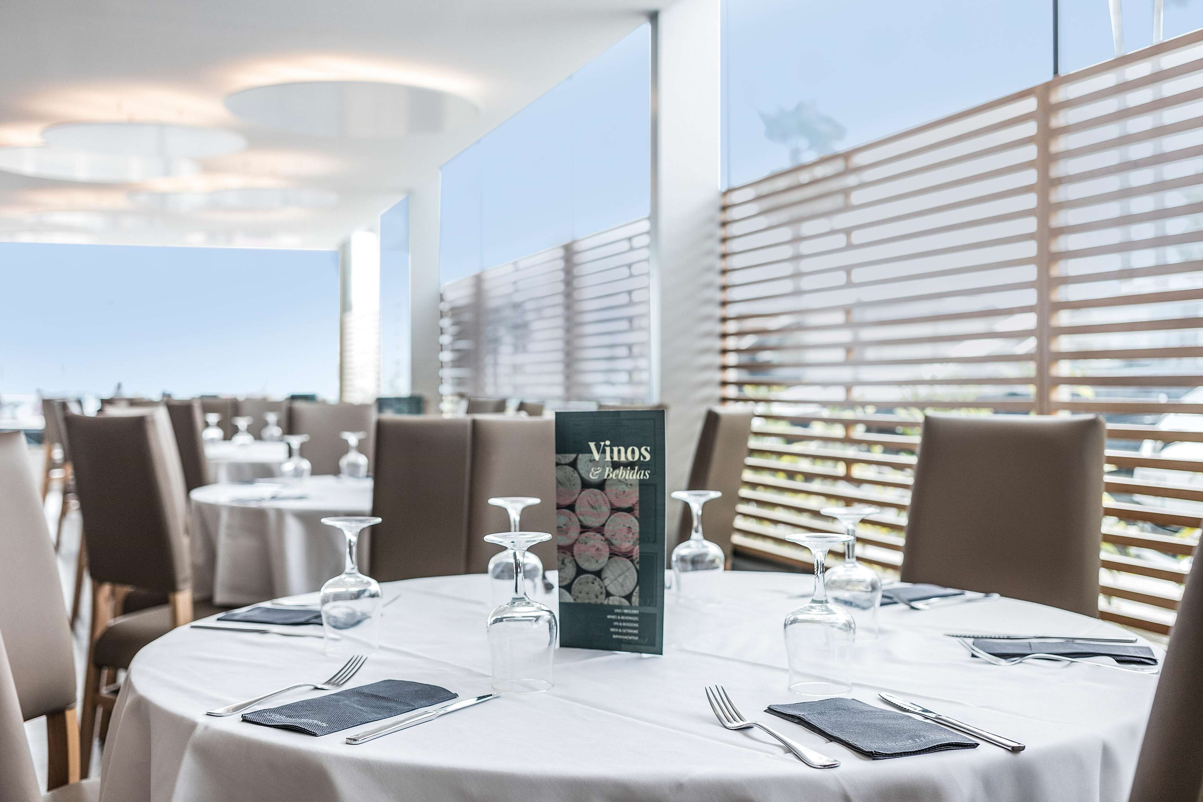 Un restaurante con mesas redondas, cada una con cubiertos, copas de vino y un atril para menús.