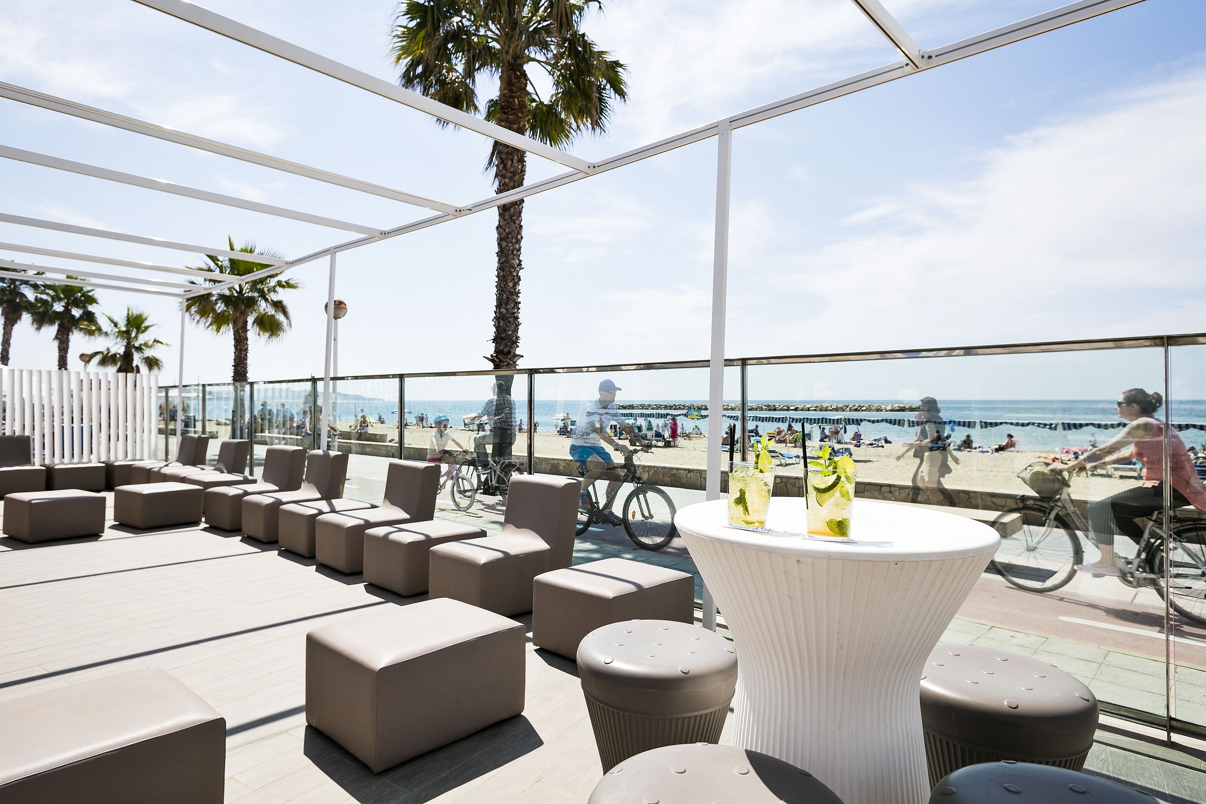 Una terrazza panoramica con posti a sedere all'aperto, un tavolo con bevande e vista sulla spiaggia e sull'oceano.