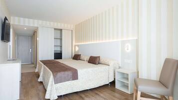 Un dormitorio con cama, mesitas de noche, una silla y televisión.